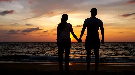 couple walking on beach coast to ocean at sunset
