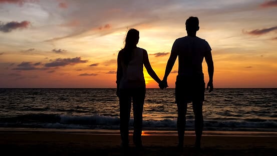 couple walking on beach coast to ocean at sunset